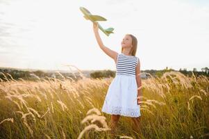 pequeno menina jogando com brinquedo avião dentro a campo foto