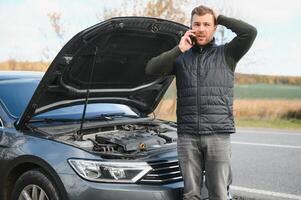 bonito jovem homem chamando para assistência com dele carro quebrado baixa de a beira da estrada foto