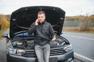 bonito jovem homem chamando para assistência com dele carro quebrado baixa de a beira da estrada foto