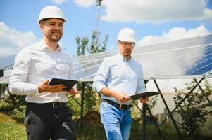 a solar Fazenda solar painel com dois engenheiros andar para Verifica a Operação do a sistema, alternativo energia para conservar a os mundos energia, fotovoltaico módulo idéia para limpar \ limpo energia Produção foto
