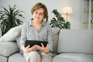 sorridente Senior mulher às casa conectado em Internet foto