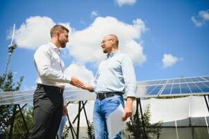 trabalhadores tremendo mãos em uma fundo do solar painéis em solar poder plantar foto