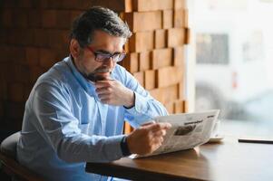 ativo Senior homem lendo jornal e bebendo café dentro restaurante foto