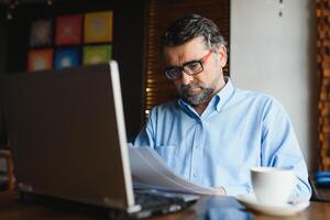 negócios, tecnologia e pessoas conceito , Senior homem de negocios com computador portátil computador bebendo café às moderno cafeteria. foto