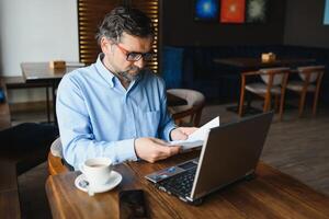 negócios, tecnologia e pessoas conceito , Senior homem de negocios com computador portátil computador bebendo café às moderno cafeteria. foto