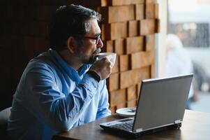 negócios, tecnologia e pessoas conceito , Senior homem de negocios com computador portátil computador bebendo café às moderno cafeteria. foto