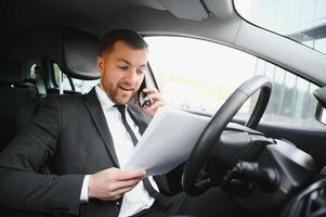 sempre dentro uma pressa. bonito jovem homem dentro cheio terno sorridente enquanto dirigindo uma carro. foto