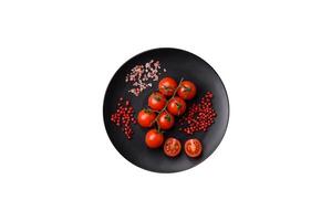 uma ramo do cru cereja tomates com sal e especiarias em uma Sombrio fundo foto