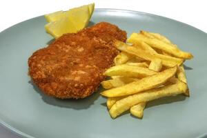 panado bife com francês fritas, dois limão cunhas, servido em uma turquesa placa. isolado dentro uma branco fundo. foto