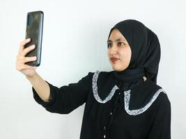 lindo jovem ásia mulher vestindo hijab sorridente e selfie levando As fotos de dela Móvel telefone