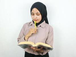 retrato lindo ásia mulher dentro hijab segurando livro e caneta, pensando sobre algo. foto