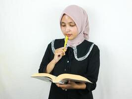 retrato lindo ásia mulher dentro hijab segurando livro e caneta, pensando sobre algo. foto