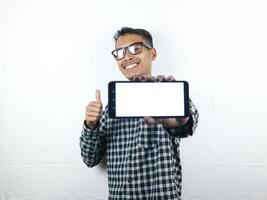 retrato do ásia homem segurando em branco tela mão telefone enquanto dando polegares acima com sorridente expressão foto