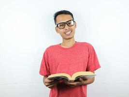 bonito ásia homem sorridente e segurando e lendo livro dentro mão foto