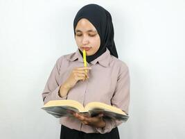 retrato lindo ásia mulher dentro hijab segurando livro e caneta, pensando sobre algo. foto