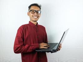 retrato do a ásia homem vestindo uma vermelho roupas segurando uma computador portátil com uma sorridente face expressão. foto