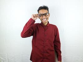 retrato ásia homem vestindo uma vermelho camisa sorrisos enquanto segurando óculos foto