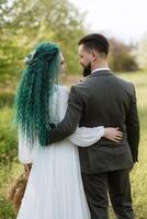 uma barbudo noivo e uma menina com verde cabelo estão caminhando foto