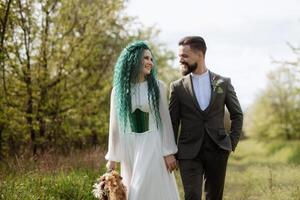 uma barbudo noivo e uma menina com verde cabelo estão caminhando foto
