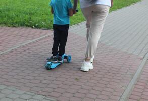 afundou petrsburgo Rússia - 08 15 2023 mãe Socorro dela filho passeio com pontapé lambreta. feliz família mãe ensina criança filho para passeio uma lambreta dentro a parque. Apoio, suporte infância paternidade ideia. foto