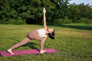 vertical tiro do jovem coreano mulher fazendo ioga Treinamento em borracha esteira, fazer asana exercícios em fresco ar dentro parque foto