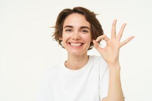 fechar acima retrato do satisfeito, sorridente jovem mulher, mostra OK, Está bem gesto, recomenda algo, dá positivo opinião, diz sim, branco fundo foto