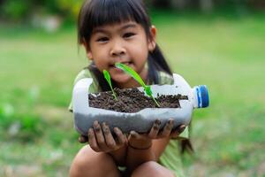 pequeno menina mostra mudas crescido dentro reciclado plástico garrafas. reciclar água garrafa Panela, jardinagem Atividades para crianças. reciclando do plástico desperdício foto