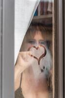 feliz e dentro amor mulher desenhando uma coração forma em a vidro do uma janela foto
