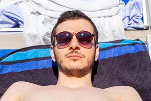 retrato do jovem homem vestindo oculos de sol e bronzeamento dentro verão foto