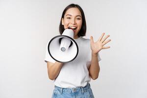 feliz ásia mulher gritando às megafone, fazer anúncio, publicidade algo, em pé sobre branco fundo foto