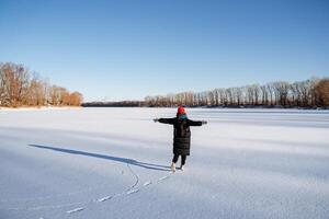 uma jovem menina dentro uma brilhante chapéu anda em em uma congeladas lago. deleite e alegria a partir de a inverno panorama com brilhante sol, Claro céu. andar dentro natureza. foto