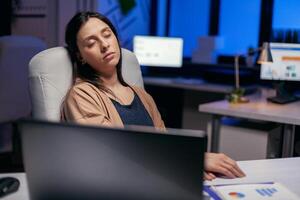 estressado cansado empresária dormindo dentro esvaziar escritório dentro a curso do trabalhando ao longo do tempo. empregado queda adormecido enquanto trabalhando atrasado às noite sozinho dentro a escritório para importante companhia projeto. foto