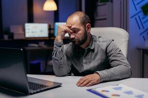 sobrecarregado homem de negocios dormindo em repouso dele cabeça em dele mão. viciado em trabalho empregado queda adormecido Porque do trabalhando atrasado às noite sozinho dentro a escritório para importante companhia projeto. foto