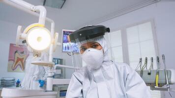 paciente pov do dentista explicando dentes tratamento vestindo cobiçado protetora terno dentro Novo normal estomatológico escritório. estomatologista dentro segurança engrenagem contra coronavírus durante heatlhcare Verifica do paciente. foto