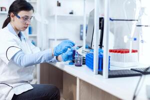 mulher cientista dentro cuidados de saúde indústria levando amostra a partir de teste tubo usando vidro pipeta. química cientista dentro estéril laboratório usando moderno tecnologia para teste microbiologia líquido. foto