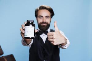 mensageiro recomenda garrafa do pílulas para Socorro com imune sistema em Câmera, mostrando jarra do vitaminas para assistência médica. profissional empregado usa suplementos dentro estúdio com azul fundo. foto