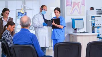 dental especialista Falando com assistente em pé dentro esperando quarto do estomatológico clínica antes pacientes exame, enfermeira levando notas em prancheta, enquanto médico olhando em tábua. foto