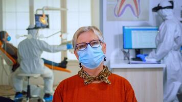 retrato do aposentado paciente dentro dental escritório olhando em Câmera vestindo face mascarar sentado em cadeira dentro esperando quarto clínica enquanto médico trabalhando. conceito do Novo normal dentista Visita dentro coronavírus surto. foto