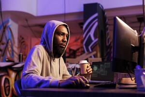 hacker bebendo café para ir enquanto fazendo Criminoso atividade em computador tarde. africano americano homem hacking rede sistema e programação Internet vírus malicioso Programas às noite foto