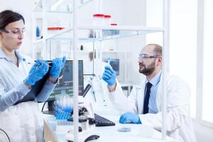 jovem homem cientista olhando pensativo às químico solução dentro teste tubos. equipe do químico químicos trabalhando juntos dentro estéril microbiologia laboratório fazendo pesquisar. foto