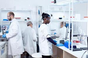 africano cientista e dela colegas fazendo experimentos dentro estéril laboratório. multiétnico equipe do pesquisadores trabalhando dentro microbiologia laboratório teste solução para médico propósito. foto