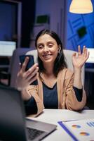 dizendo Olá dentro a curso do teleconferência com empreendedores fazendo ao longo do tempo. mulher trabalhando em finança durante uma vídeo conferência com colegas de trabalho às noite horas dentro a escritório. foto