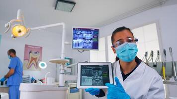 paciente pov dentro dental escritório discutindo tratamento do dentes cavidade, dentista apontando em digital raio X usando tábua. equipe do médicos trabalhando dentro moderno estomatológico clínica, explicando radiografia dente foto