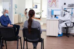 mulher paciente dentro odontologia escritório esperando para diagnóstico dentro dental clínica corredor. dentista e funcionários vestido dentro ppe terno consultando paciente. o preenchimento saúde forma. foto