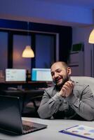 empreendedor sorridente durante o negócio vídeo ligar com alguém,. atrasado às noite. homem de negocios dentro a curso do a importante vídeo conferência enquanto fazendo hora extra às a escritório. foto