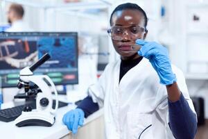 concentrado Visão do médico africano cientista segurando vidro microscópio vidro. Preto cuidados de saúde cientista dentro bioquímica laboratório vestindo estéril equipamento. foto