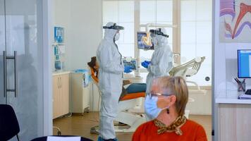 médicos vestindo cheio vírus proteção uniforme em pé dentro cirurgia quarto planejamento dental tratamento enquanto idosos pacientes esperando dentro recepção guardando distância. conceito do Novo normal dentista Visita foto