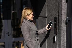 mulher travamento cadeado inteligente em a Entrada porta usando uma inteligente telefone. conceito do usando inteligente eletrônico fechaduras com sem chave Acesso foto