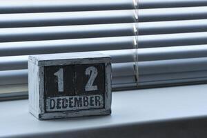 manhã dezembro 12 em de madeira calendário em pé em janela com persianas. foto
