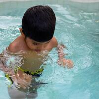 feliz indiano Garoto natação dentro uma piscina, criança vestindo natação traje ao longo com ar tubo durante quente verão Férias, crianças Garoto dentro grande natação piscina. foto